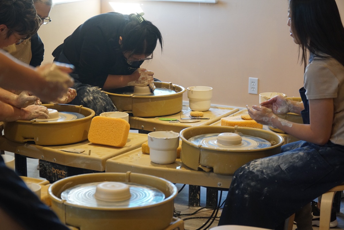 Multiple students throwing pottery on Brent wheels at Olomana Studios