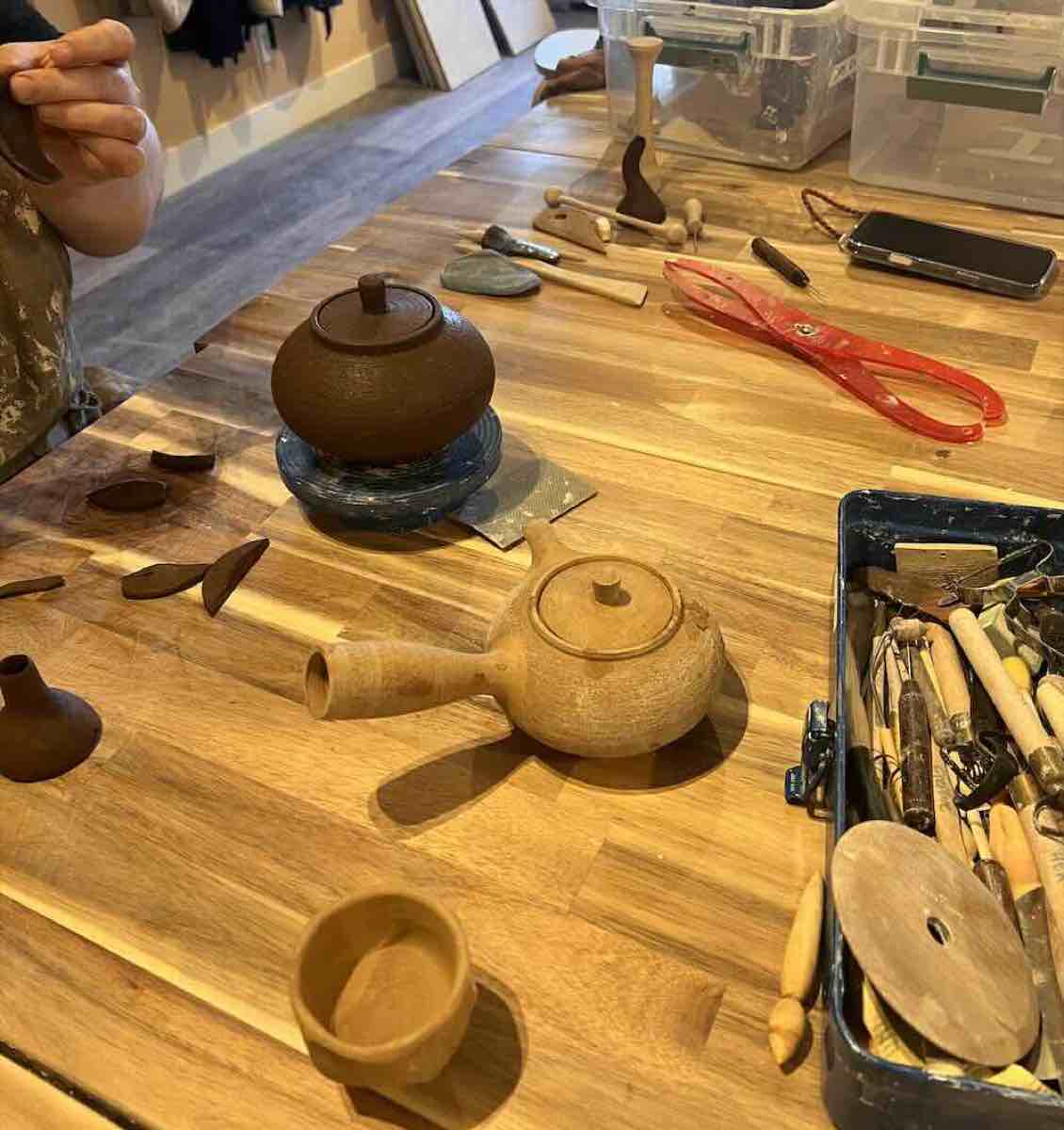 Bisque-fired teapots and yunomi cups on the workbench with pottery tools